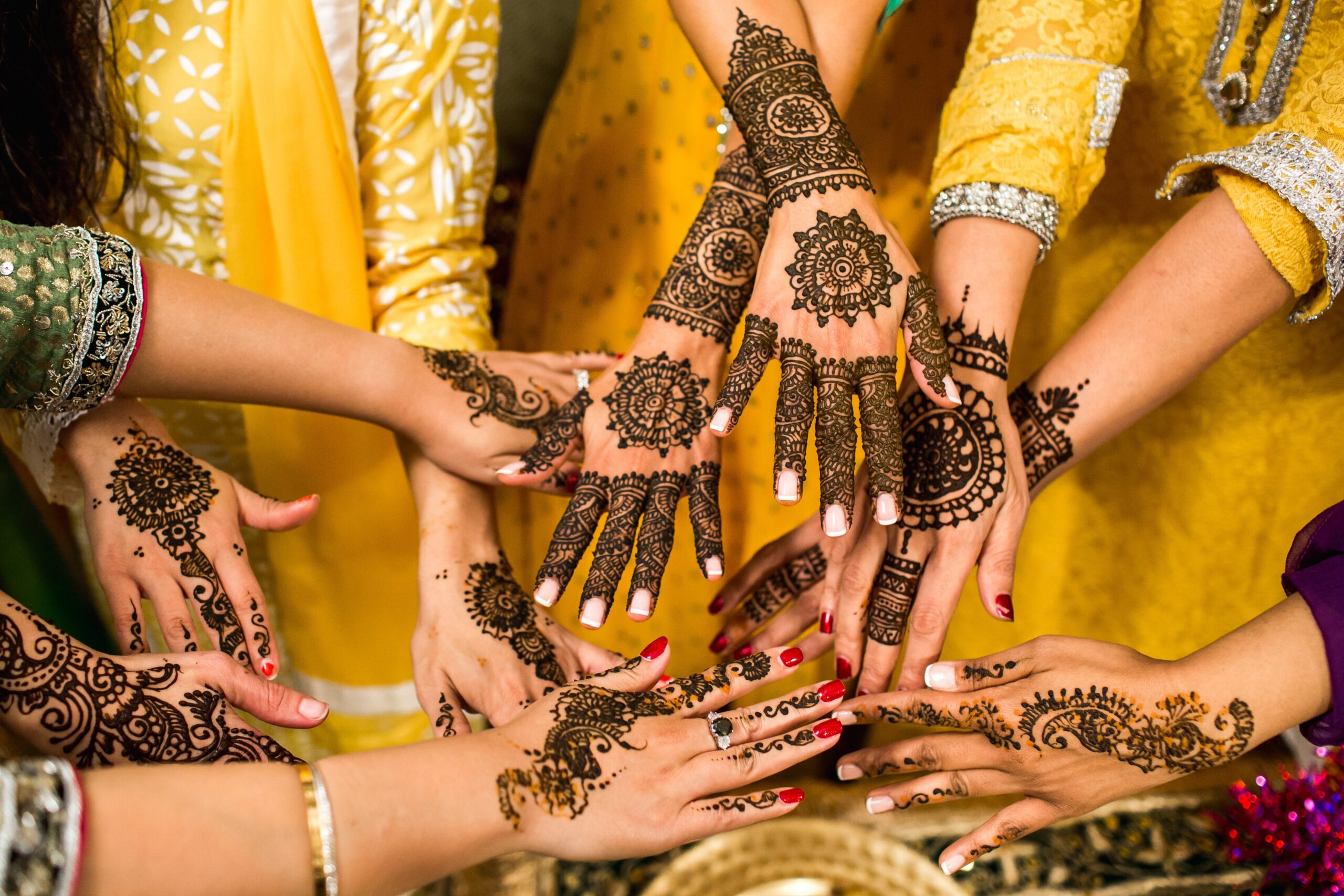 Depicts several women's hands with mehendi or henna tattoos.